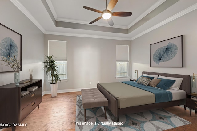 bedroom with a tray ceiling, multiple windows, light wood-style floors, ornamental molding, and baseboards