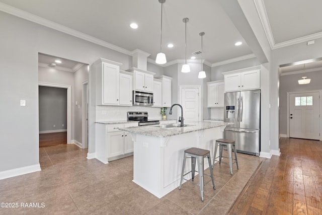 kitchen with appliances with stainless steel finishes, a sink, baseboards, a kitchen bar, and white cabinets