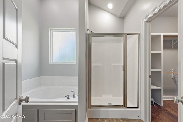 full bath featuring a stall shower, a bath, a walk in closet, and wood finished floors
