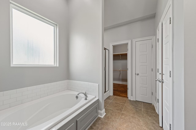 bathroom featuring a bath, tile patterned flooring, a walk in closet, a stall shower, and baseboards
