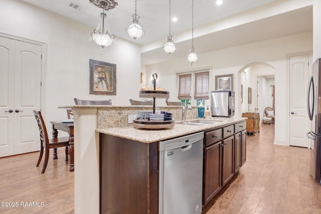 kitchen with appliances with stainless steel finishes, a sink, arched walkways, a kitchen island with sink, and light wood finished floors