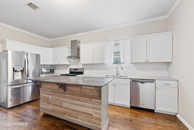 kitchen with crown molding, wall chimney range hood, white cabinets, a sink, and stainless steel appliances