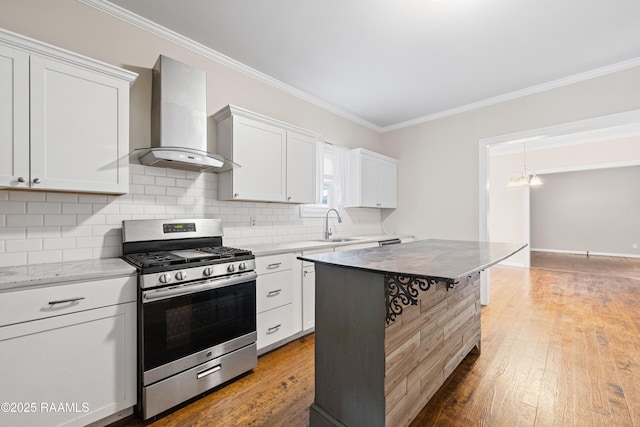 kitchen with stainless steel range with gas stovetop, ornamental molding, wall chimney exhaust hood, and wood finished floors