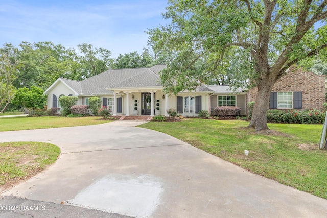 single story home featuring a porch, a shingled roof, a front lawn, and curved driveway