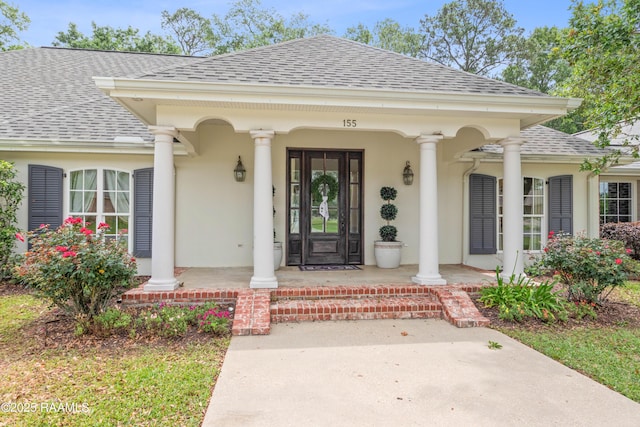 view of exterior entry with a porch, a shingled roof, and stucco siding