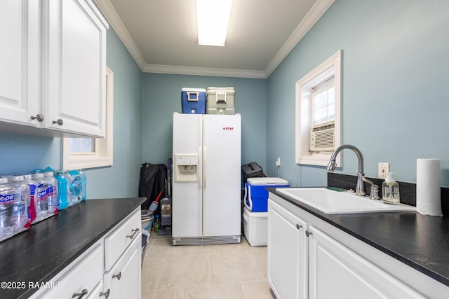 kitchen with crown molding, dark countertops, a sink, white refrigerator with ice dispenser, and white cabinetry