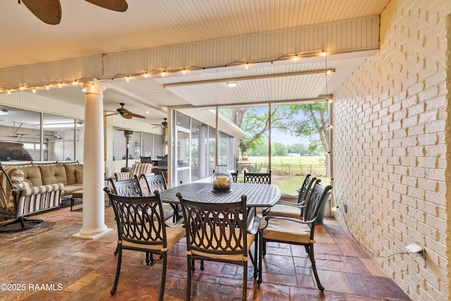 dining space with brick wall, ceiling fan, ornate columns, and stone tile flooring
