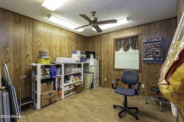 office area with wood walls, ceiling fan, a textured ceiling, and wood finished floors