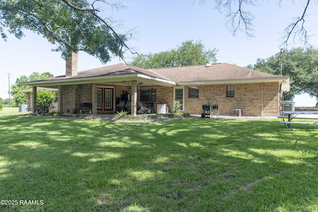 back of property with a yard, a patio area, a chimney, and brick siding
