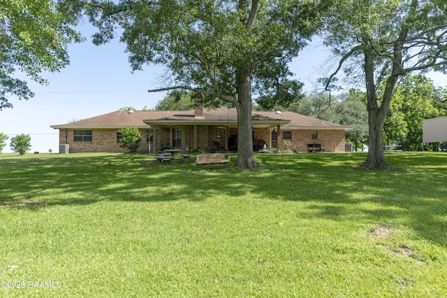 rear view of property featuring a chimney, brick siding, and a lawn