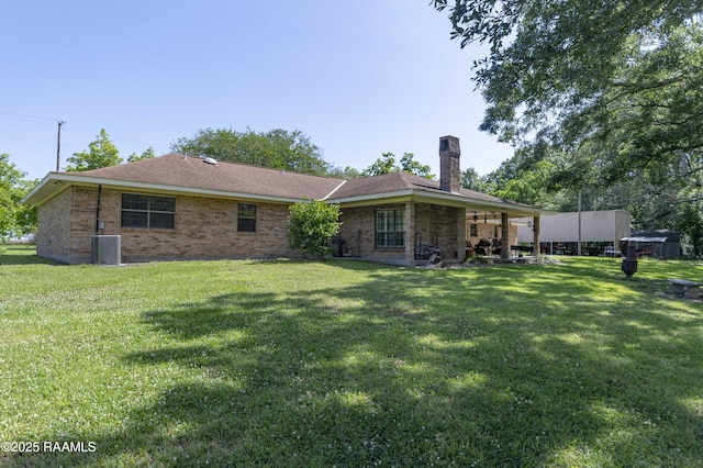 back of property with a chimney, a yard, brick siding, and central air condition unit