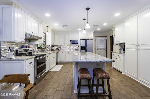 kitchen with a center island, white cabinetry, under cabinet range hood, appliances with stainless steel finishes, and tasteful backsplash