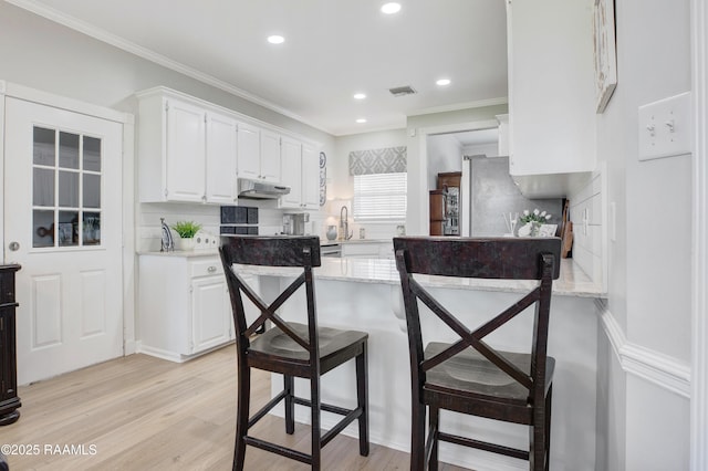 502 River Woods Dr, Lafayette, LA 70508 - kitchen featuring under cabinet range hood, white cabinets, a peninsula, a breakfast bar area, and light wood finished floors