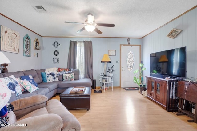 living room with a ceiling fan, light wood-type flooring, visible vents, a textured ceiling, and ornamental molding