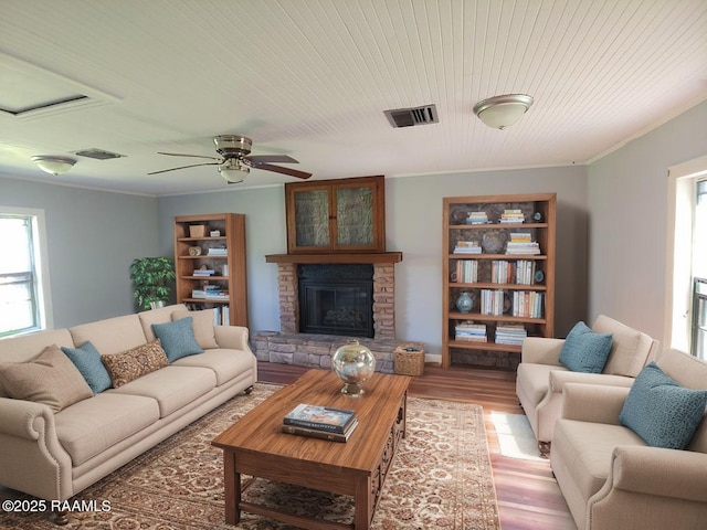 living area with ceiling fan, visible vents, crown molding, a fireplace, and light wood-style flooring