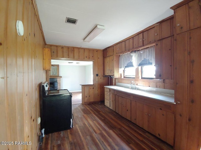 kitchen featuring wooden walls, brown cabinets, a sink, dark wood finished floors, and visible vents