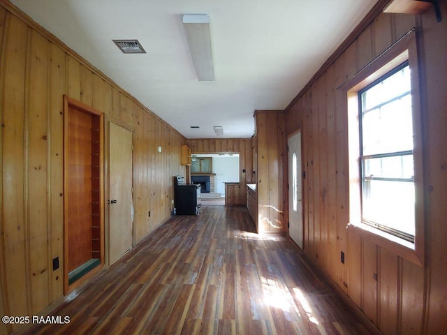 unfurnished living room featuring wooden walls, a fireplace with raised hearth, a healthy amount of sunlight, and wood finished floors