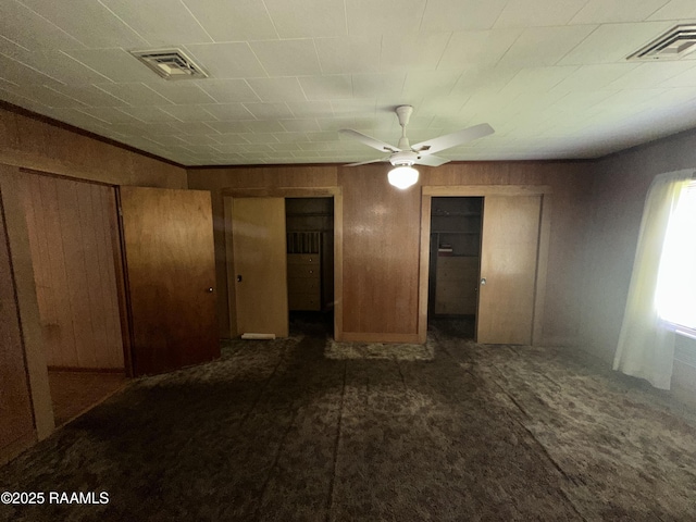 unfurnished bedroom with visible vents, wood walls, dark carpet, and a ceiling fan