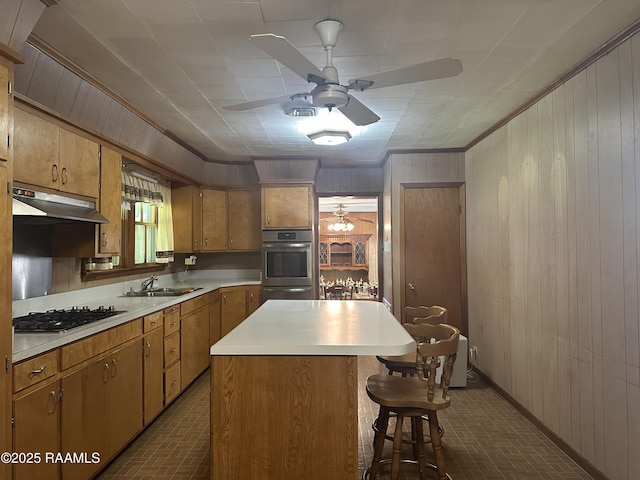 kitchen featuring wooden walls, ceiling fan, a sink, brick patterned floor, and gas stovetop