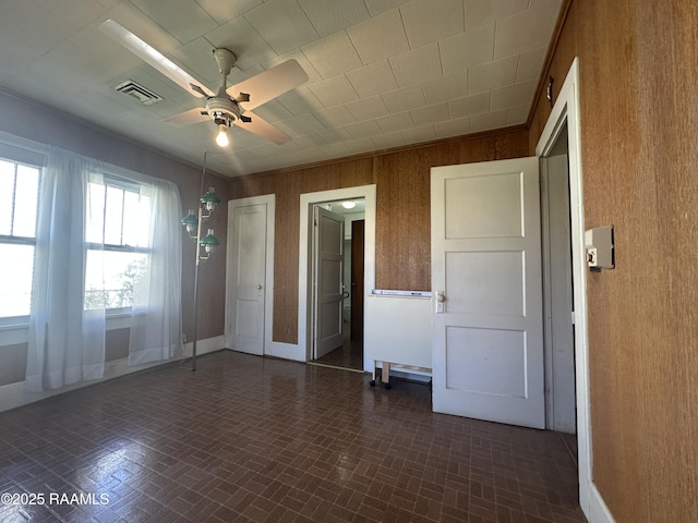 empty room with visible vents, wooden walls, ceiling fan, and brick patterned floor