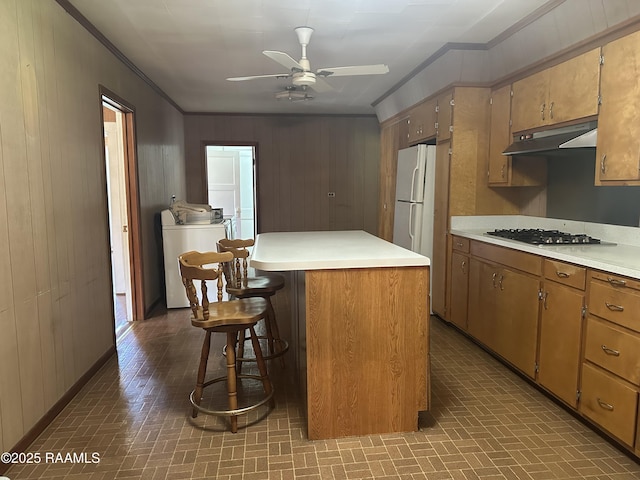 kitchen featuring ornamental molding, brick patterned floor, washer and clothes dryer, under cabinet range hood, and stainless steel gas stovetop