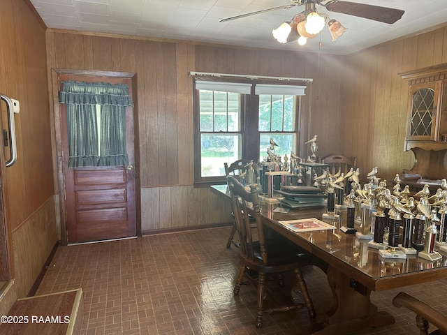 dining area with a ceiling fan, wooden walls, and brick patterned floor