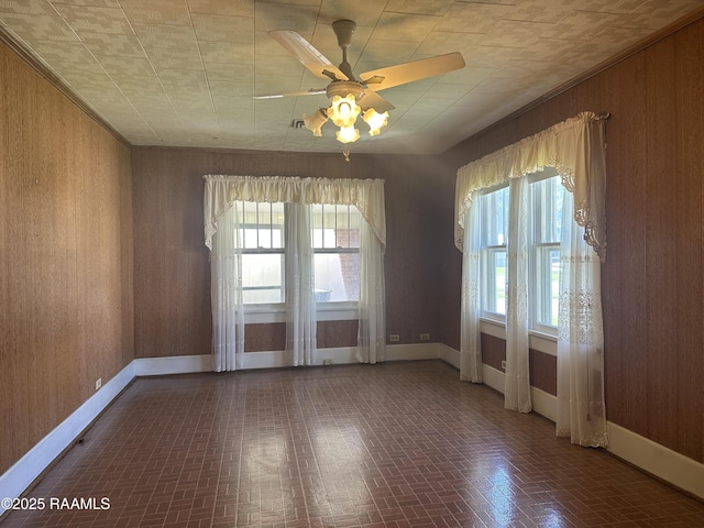 spare room featuring ceiling fan, brick patterned floor, wood walls, and baseboards