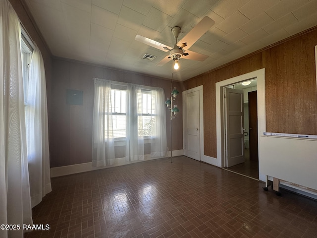 unfurnished room with visible vents, wooden walls, ceiling fan, and brick patterned floor