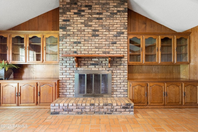 319 Roger Rd, Lafayette, LA 70507 - unfurnished living room featuring lofted ceiling, wood walls, a textured ceiling, brick floors, and a brick fireplace