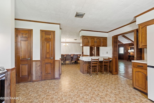 319 Roger Rd, Lafayette, LA 70507 - kitchen with a breakfast bar area, a wainscoted wall, light countertops, ornamental molding, and a chandelier