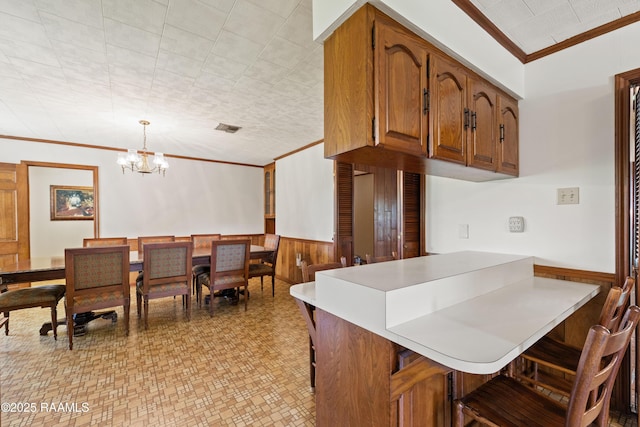 319 Roger Rd, Lafayette, LA 70507 - kitchen with crown molding, a breakfast bar, a wainscoted wall, light countertops, and brown cabinetry