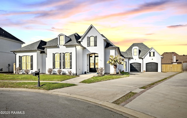 french country home featuring driveway, french doors, a garage, fence, and a yard