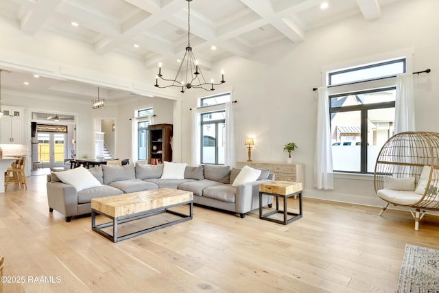 living area with light wood-type flooring, a towering ceiling, beam ceiling, and a wealth of natural light