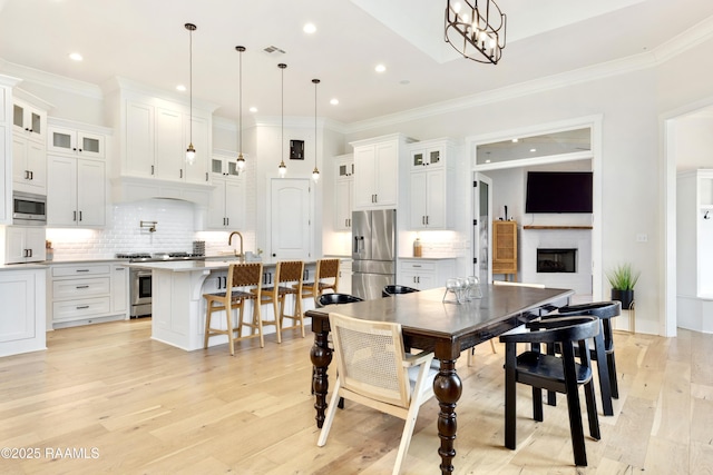 dining area with recessed lighting, crown molding, light wood-style floors, and a glass covered fireplace