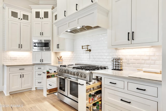 kitchen with decorative backsplash, white cabinets, custom exhaust hood, stainless steel appliances, and light wood-style flooring