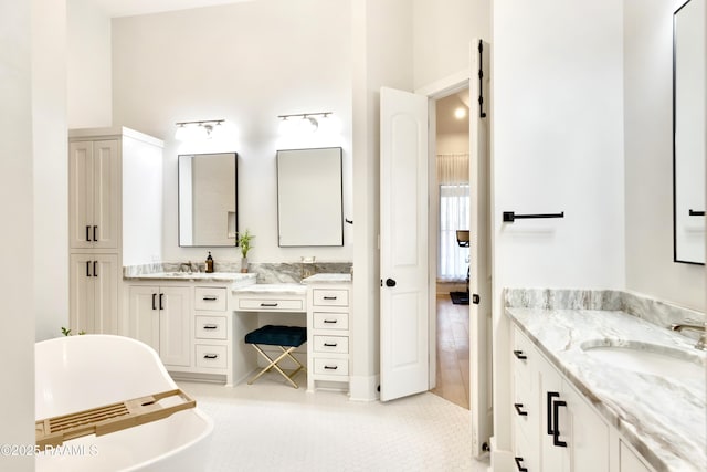 bathroom with a freestanding bath, a high ceiling, a sink, and two vanities