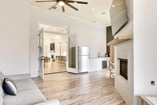 living area with crown molding, light wood finished floors, a fireplace, a ceiling fan, and recessed lighting