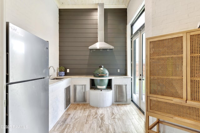 kitchen featuring light wood-type flooring, freestanding refrigerator, a sink, and wall chimney exhaust hood