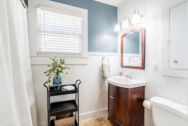 full bathroom with toilet, vanity, and a wainscoted wall