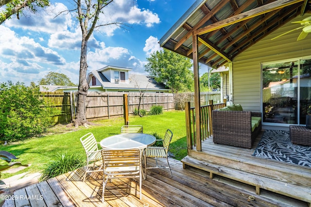 wooden terrace featuring a lawn, outdoor dining space, and a fenced backyard