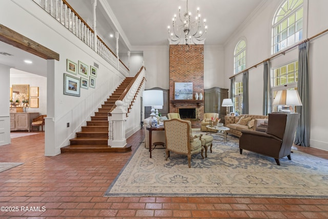 living area with a notable chandelier, crown molding, a towering ceiling, brick floor, and stairs