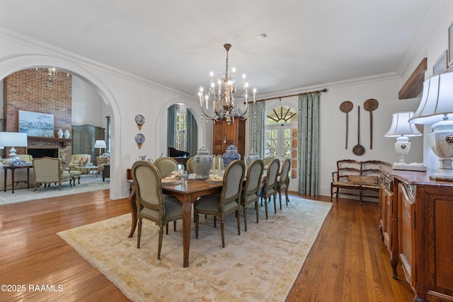 dining room with arched walkways, ornamental molding, an inviting chandelier, and wood finished floors