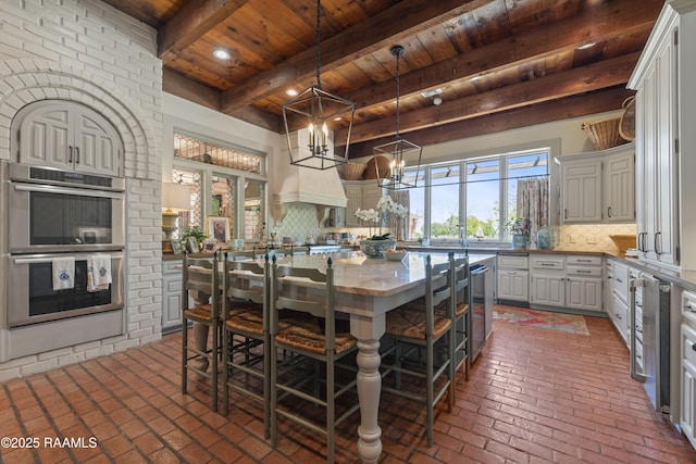 kitchen with brick floor, stainless steel double oven, wooden ceiling, backsplash, and a kitchen island