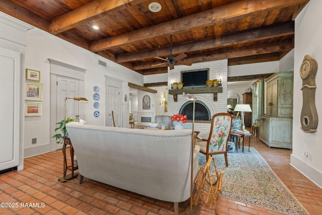 living room featuring wood ceiling, beam ceiling, a fireplace, ceiling fan, and brick floor