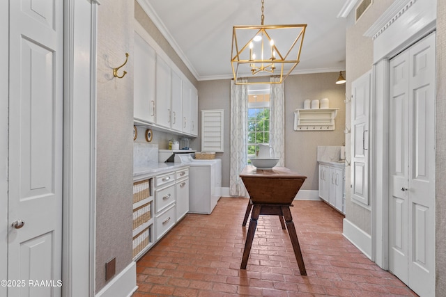 kitchen featuring washer / clothes dryer, brick floor, crown molding, an inviting chandelier, and white cabinetry