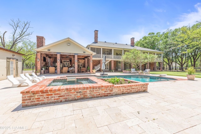 rear view of property with a chimney, an outdoor pool, stairs, a patio area, and an in ground hot tub