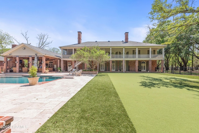back of property with fence, brick siding, a balcony, a patio, and a fenced in pool