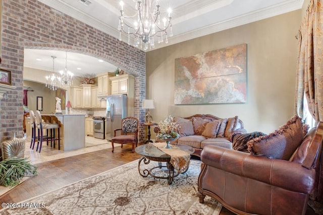 living area with a fireplace, a notable chandelier, crown molding, arched walkways, and light wood-style floors