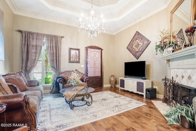 living room with a tray ceiling, an inviting chandelier, crown molding, wood finished floors, and a tile fireplace