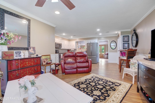 living area with light wood finished floors, crown molding, a ceiling fan, and a wainscoted wall